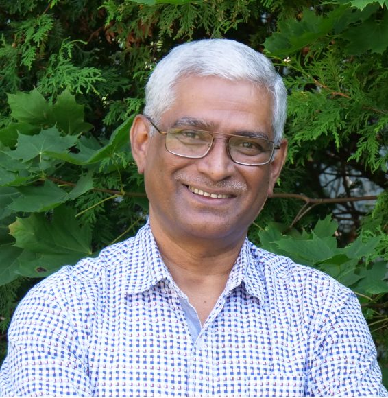 Dr Hemant Gupta smiling in front of green foliage